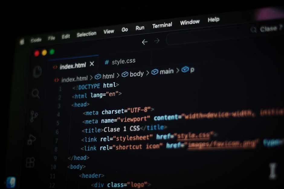 Close-up image of a person's right hand typing on a laptop keyboard placed on a wooden surface. The laptop screen displays lines of code in various colors on a dark background. The individual is weari